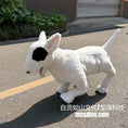 Load image into Gallery viewer, A white bull dog plush toy with a black patch on its face, standing on an asphalt street outdoors.