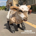 Bild in Galerie-Betrachter laden, A large plush goat or sheep toy with brown, white, and gray fur stands on an outdoor paved street in front of buildings. The toy has long ears, a textured fur coat, and dark gray hooves.