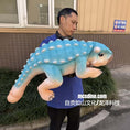 Load image into Gallery viewer, Person holding a large blue and pink plush dinosaur toy outdoors.