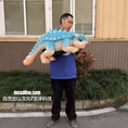 Load image into Gallery viewer, Man holding a large blue and beige dinosaur plush toy outdoors.