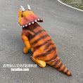 Load image into Gallery viewer, A realistic orange and brown striped Triceratops dinosaur costume or prop shown from the back on an asphalt surface. The costume features a textured skin-like finish, three horns on the head, and a tail, with a watermark at the bottom left.