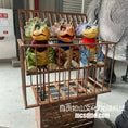 Load image into Gallery viewer, Three colorful dinosaur plush toys in a wooden cage with a person partially visible in the background.
