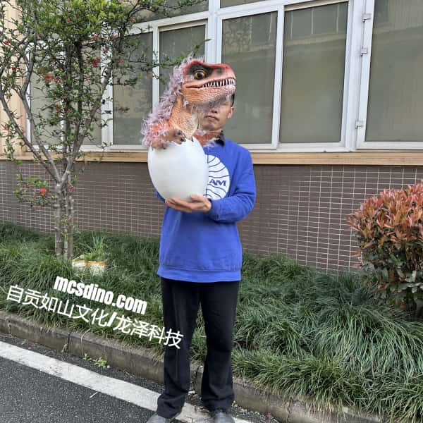 Person wearing a dinosaur head mask holding a ball with a building and plants in the background
