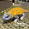 Load image into Gallery viewer, Toy dinosaur with a yellow shell on a paved surface
