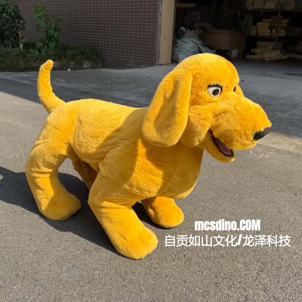 A yellow plush dog costume or stuffed animal toy standing on an outdoor paved surface, with a building and plants in the background. White Chinese text watermark is visible near the bottom right.