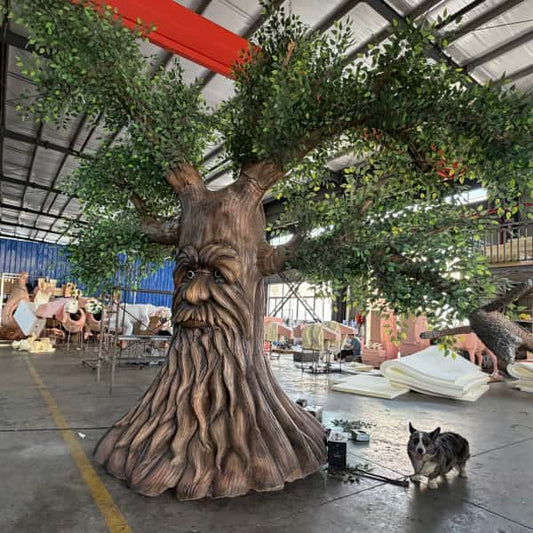 Large tree-like sculpture with a face in an indoor setting, possibly a warehouse, with a dog standing nearby.