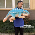 Load image into Gallery viewer, Person holding a large blue and beige dinosaur plush toy outdoors.
