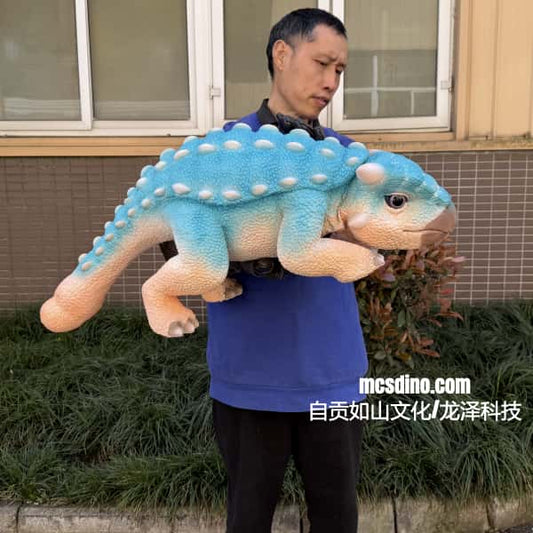 Person holding a large blue and beige dinosaur plush toy outdoors.