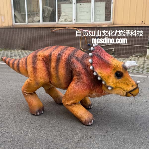 A realistic animatronic dinosaur toy, specifically a Triassic period dinosaur with orange and black stripes, walking on an outdoor paved surface in front of a building.