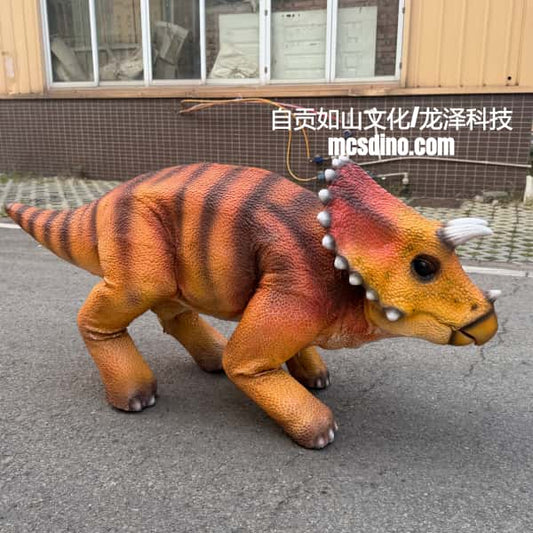 A realistic animatronic dinosaur toy, specifically a Triassic period dinosaur with orange and black stripes, walking on an outdoor paved surface in front of a building.