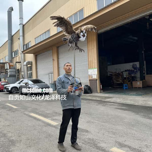 Man holding a remote control with an owl flying nearby in front of a building.