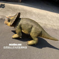 Load image into Gallery viewer, A realistic toy or model Triceratops dinosaur with a textured olive-green and tan body, standing on asphalt outdoors. The watermark 'mcsdino.
