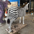 Carica l'immagine nel visualizzatore della galleria, A zebra animal statue or model shown indoors on a concrete floor, with black-and-white stripes, a brown mane, and a power cord visible near its feet. A dinosaur figure is partially visible in the background.
